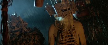 Movie still from “Quest for Fire” (1981), directed by Jean-Jacques Annaud – A man with a long beard is wearing a mask; Medium shot, Low angle