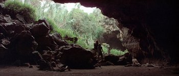 Movie still from “Quest for Fire” (1981), directed by Jean-Jacques Annaud – Two people are standing in a cave looking out into the woods; Extreme Wide shot, Low angle