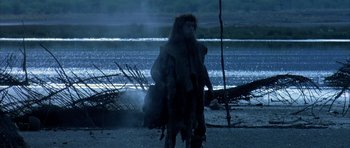 Movie still from “Quest for Fire” (1981), directed by Jean-Jacques Annaud – A man dressed as a werewolf standing in front of a body of water at night; Wide shot, Low angle