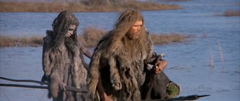 Movie still from “Quest for Fire” (1981), directed by Jean-Jacques Annaud – Two people dressed in animal skins walking by a body of water; Medium shot, Low angle
