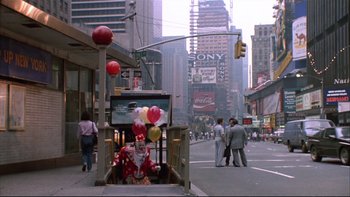 Movie still from “Quick Change” (1990), directed by Howard Franklin – A street scene with a clown sitting on the side of the street; Extreme Wide shot, High angle