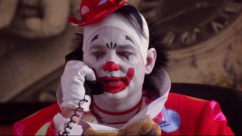 Movie still from “Quick Change” (1990), directed by Howard Franklin – A clown is talking on a phone while wearing a red hat; Close Up shot, High angle