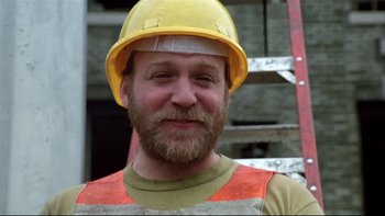 Movie still from “Quick Change” (1990), directed by Howard Franklin – A man with a beard wearing a yellow hard hat; Close Up shot, Low angle