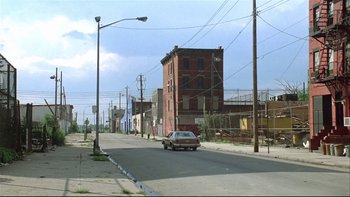 Movie still from “Quick Change” (1990), directed by Howard Franklin – A car driving down a street next to an old brick building; Extreme Wide shot, High angle