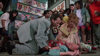 Movie still from “Quick Change” (1990), directed by Howard Franklin – A group of people standing around a man laying on the ground; Wide shot, Low angle
