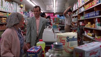 Movie still from “Quick Change” (1990), directed by Howard Franklin – A man standing in front of a store with other people; Medium shot, Over the shoulder angle