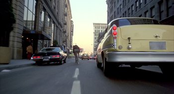 Movie still from “Quicksilver” (1986), directed by Thomas Michael Donnelly – A man riding a bike down a street next to cars; Wide shot, Low angle