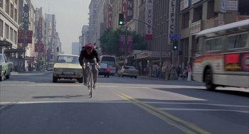 Movie still from “Quicksilver” (1986), directed by Thomas Michael Donnelly – A man riding a bike down the middle of a street; Wide shot, Low angle