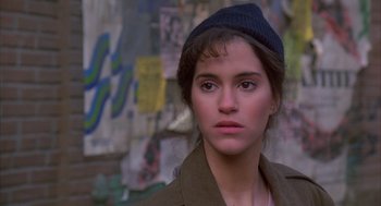 Movie still from “Quicksilver” (1986), directed by Thomas Michael Donnelly – A woman with a hat is standing in front of a wall; Close Up shot, High angle