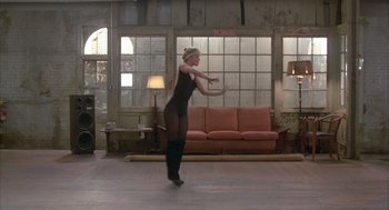 Movie still from “Quicksilver” (1986), directed by Thomas Michael Donnelly – A woman in a black dress dancing in front of a couch; Wide shot, Low angle