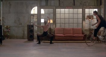 Movie still from “Quicksilver” (1986), directed by Thomas Michael Donnelly – A man is performing a dance in front of a couch; Wide shot, High angle