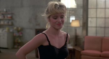 Movie still from “Quicksilver” (1986), directed by Thomas Michael Donnelly – A woman in a black top is standing in front of a wall; Close Up shot, Over the shoulder angle