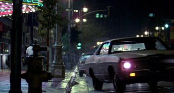 Movie still from “Quicksilver” (1986), directed by Thomas Michael Donnelly – Cars are driving down a street at night; Wide shot, Low angle