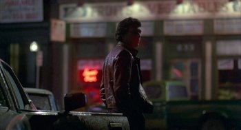 Movie still from “Quicksilver” (1986), directed by Thomas Michael Donnelly – A man standing next to a car in a parking lot at night; Wide shot, Low angle