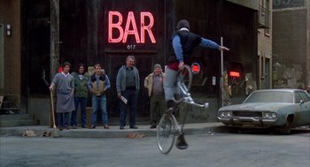 Movie still from “Quicksilver” (1986), directed by Thomas Michael Donnelly – A man riding a bike in front of a crowd of onlookers; Wide shot, Low angle