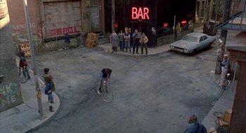 Movie still from “Quicksilver” (1986), directed by Thomas Michael Donnelly – A man riding a bike down the middle of a street; Extreme Wide shot, High angle
