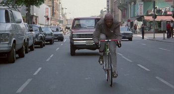 Movie still from “Quicksilver” (1986), directed by Thomas Michael Donnelly – A man riding a bike down the middle of the street; Wide shot, Low angle