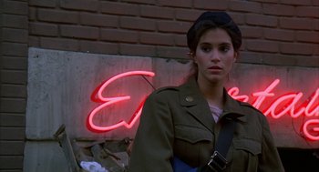 Movie still from “Quicksilver” (1986), directed by Thomas Michael Donnelly – A woman in a military jacket standing in front of a neon sign; Close Up shot, Low angle