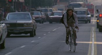 Movie still from “Quicksilver” (1986), directed by Thomas Michael Donnelly – A man riding a bike down the middle of the street; Wide shot, Low angle