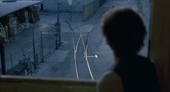 Movie still from “Quicksilver” (1986), directed by Thomas Michael Donnelly – A person sitting on a bench looking at a train track; Extreme Wide shot, High angle
