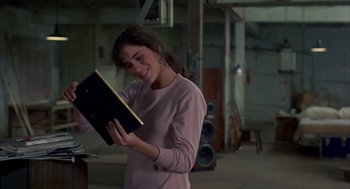 Movie still from “Quicksilver” (1986), directed by Thomas Michael Donnelly – A woman is holding a book in her hands; Medium shot, Over the shoulder angle