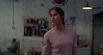 Movie still from “Quicksilver” (1986), directed by Thomas Michael Donnelly – A woman in a pink shirt is standing in front of a brick wall; Medium shot, Over the shoulder angle