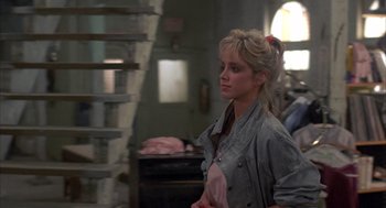 Movie still from “Quicksilver” (1986), directed by Thomas Michael Donnelly – A woman with a ponytail standing in a room; Medium shot, Over the shoulder angle