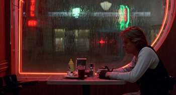 Movie still from “Quicksilver” (1986), directed by Thomas Michael Donnelly – A woman sitting at a table in front of a window; Wide shot, Low angle