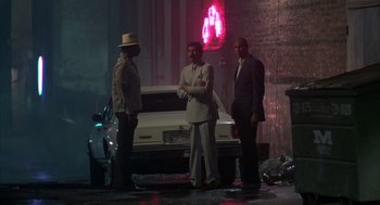 Movie still from “Quicksilver” (1986), directed by Thomas Michael Donnelly – A group of men standing next to each other near a car; Wide shot, Low angle