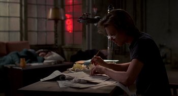 Movie still from “Quicksilver” (1986), directed by Thomas Michael Donnelly – A person sitting at a table writing on a piece of paper; Medium shot, Low angle