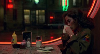 Movie still from “Quicksilver” (1986), directed by Thomas Michael Donnelly – A woman sitting at a table drinking a cup of coffee; Medium shot, High angle