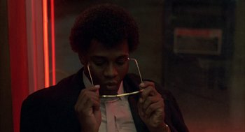 Movie still from “Quicksilver” (1986), directed by Thomas Michael Donnelly – A man holding a pair of eyeglasses up to his face; Close Up shot, Low angle