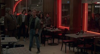 Movie still from “Quicksilver” (1986), directed by Thomas Michael Donnelly – A group of people standing in a room with tables and chairs; Wide shot, Over the shoulder angle