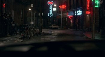 Movie still from “Quicksilver” (1986), directed by Thomas Michael Donnelly – A city street at night lit up by neon signs; Wide shot, High angle