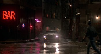 Movie still from “Quicksilver” (1986), directed by Thomas Michael Donnelly – A car driving down a street at night; Wide shot, High angle