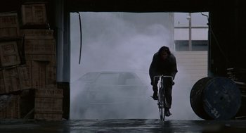 Movie still from “Quicksilver” (1986), directed by Thomas Michael Donnelly – A person riding a bike in front of a car; Wide shot, Low angle