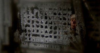 Movie still from “Quintet” (1979), directed by Robert Altman – A man is looking through a hole in a wall; Close Up shot, Low angle