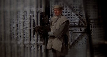 Movie still from “Quintet” (1979), directed by Robert Altman – A man standing in front of a metal fence; Medium shot, Low angle
