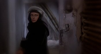 Movie still from “Quintet” (1979), directed by Robert Altman – A woman wearing a black coat and a white hat; Medium shot, Over the shoulder angle