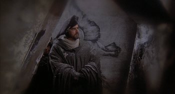 Movie still from “Quintet” (1979), directed by Robert Altman – A man wearing a black hat standing in front of a painting; Medium shot, High angle