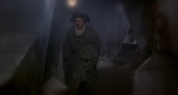 Movie still from “Quintet” (1979), directed by Robert Altman – A man wearing a coat and a hat standing in the fog; Wide shot, High angle