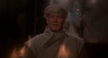 Movie still from “Quintet” (1979), directed by Robert Altman – A person wearing a hat with flames in the background; Close Up shot, Over the shoulder angle