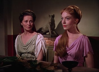 Movie still from “Quo Vadis” (1951), directed by Anthony Mann – Two women sitting at a table in front of a statue of a dog; Medium shot, Over the shoulder angle
