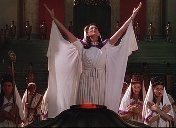 Movie still from “Quo Vadis” (1951), directed by Anthony Mann – A woman in a white dress is holding her arms up; Medium shot, Low angle