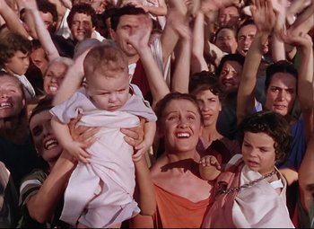 Movie still from “Quo Vadis” (1951), directed by Anthony Mann – A group of people are gathered around a woman holding a baby; Medium shot, High angle