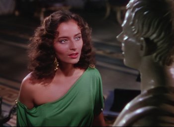 Movie still from “Quo Vadis” (1951), directed by Anthony Mann – A woman in a green dress standing next to a statue; Medium shot, Over the shoulder angle