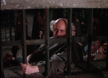 Movie still from “Quo Vadis” (1951), directed by Anthony Mann – An old man with a beard is looking through a fence; Medium shot, High angle