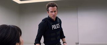 Movie still from “R.I.P.D.” (2013), directed by Robert Schwentke – A man in a police vest is standing in a room; Medium shot, Over the shoulder angle