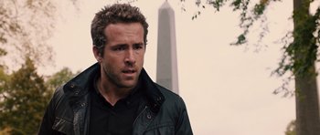 Movie still from “R.I.P.D.” (2013), directed by Robert Schwentke – A person wearing a jacket near a building; Close Up shot, Over the shoulder angle