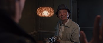Movie still from “R.I.P.D.” (2013), directed by Robert Schwentke – An older man wearing a hat and holding a box; Medium shot, Over the shoulder angle